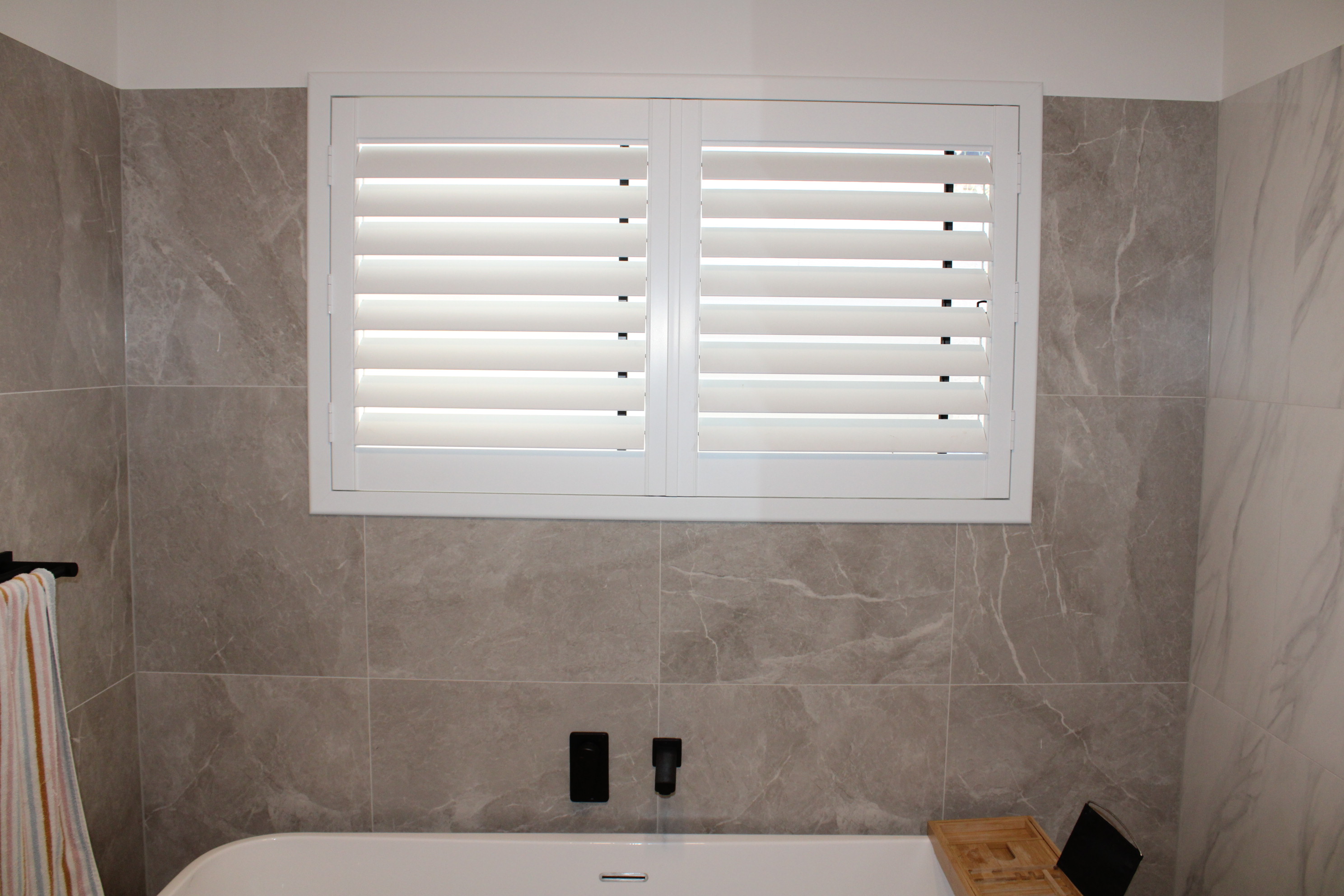 White PVC plantation shutters installed in a bathroom by DHE