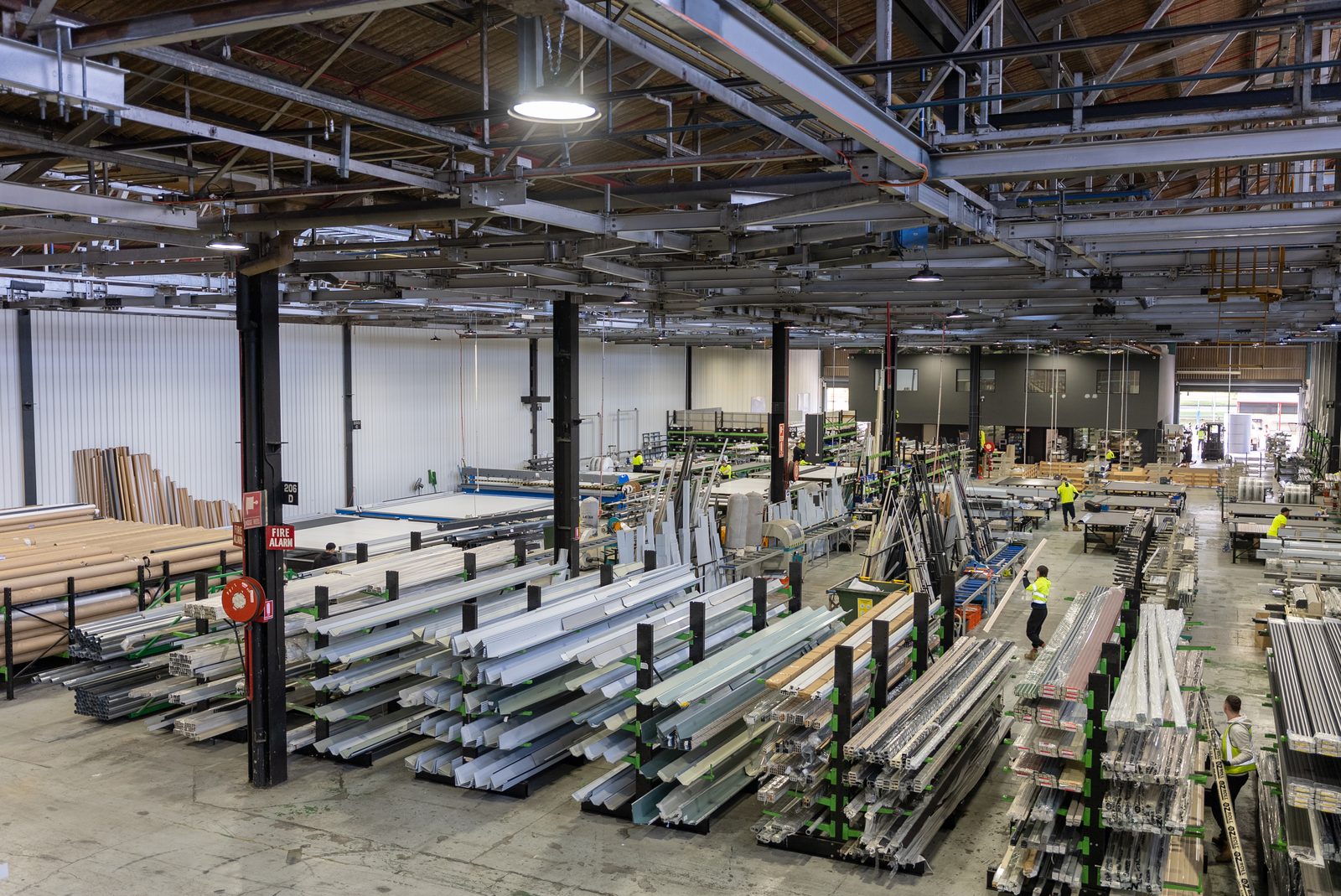 Factory floor with racks of aluminium sections, workbenches and staff in high-visibility clothing.