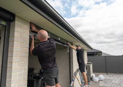 Two DHE installers fitting an outdoor blind headbox to the beam of an alfresco
