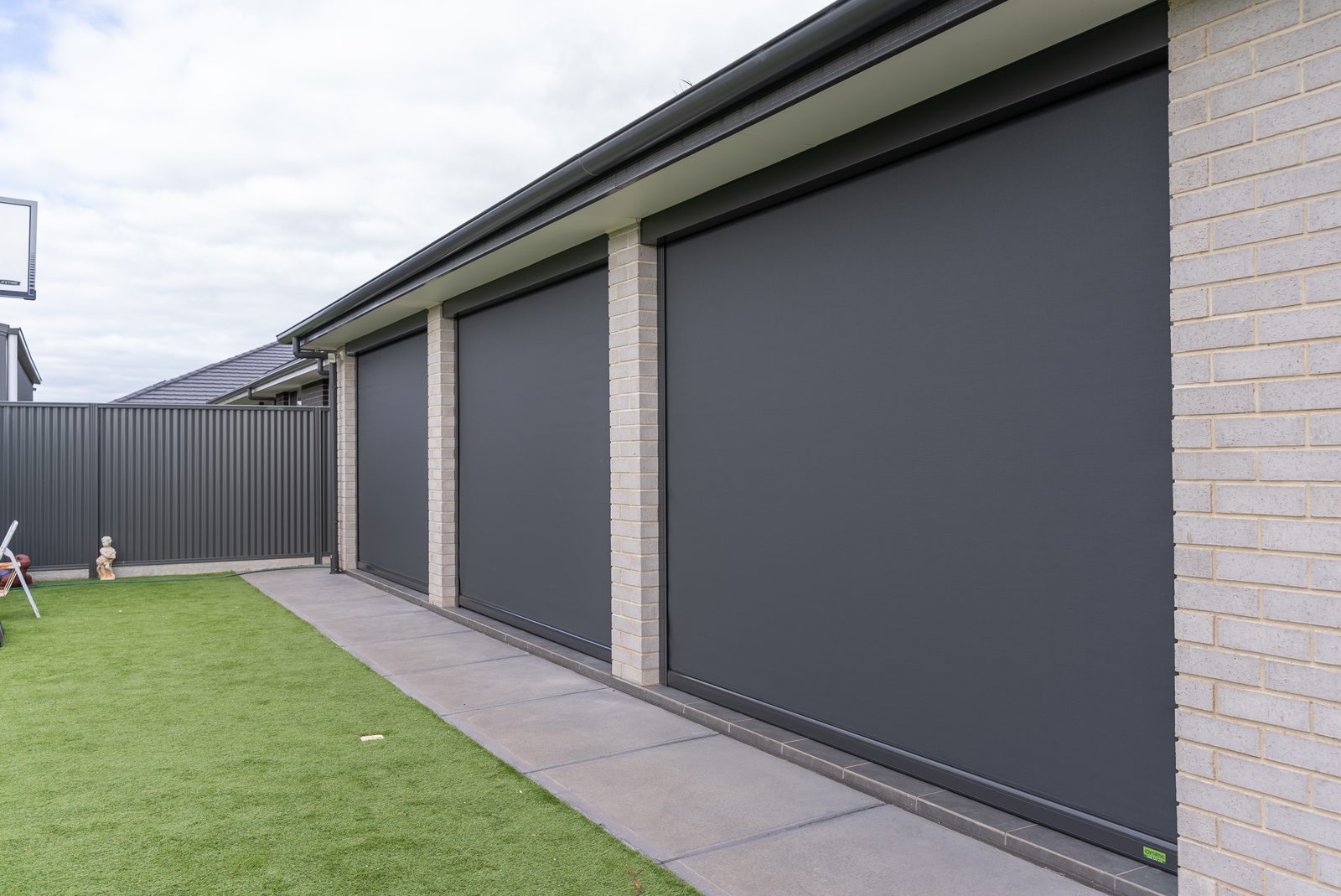 Outdoor blinds lowered down the side of a home beside the paving