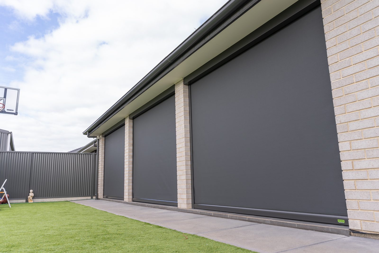 Charcoal track-guided outdoor blinds closed between brick pillars on an alfresco